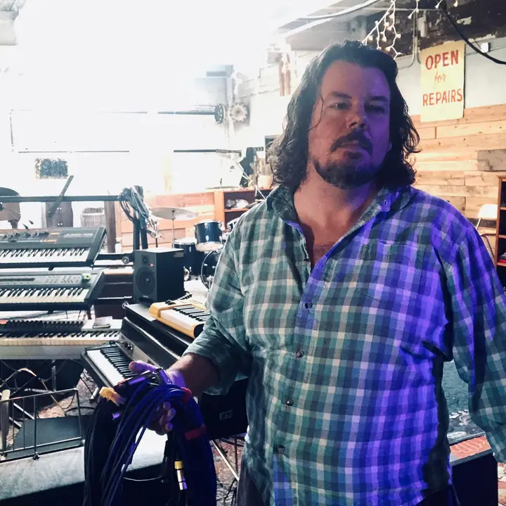 Dan McCormick holding a coil of blue cables in front of keyboards in the studio
